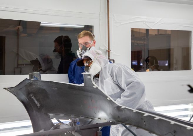 instructor and student looking car part in spray booth