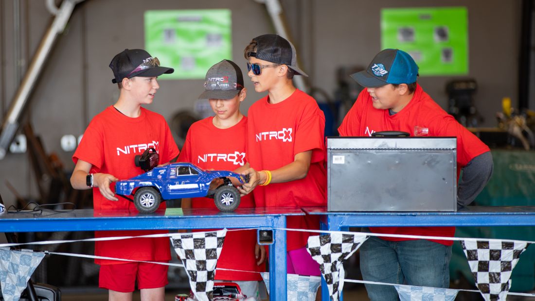 4 campers wearing Nitro-X shirts and hats working on a miniature car