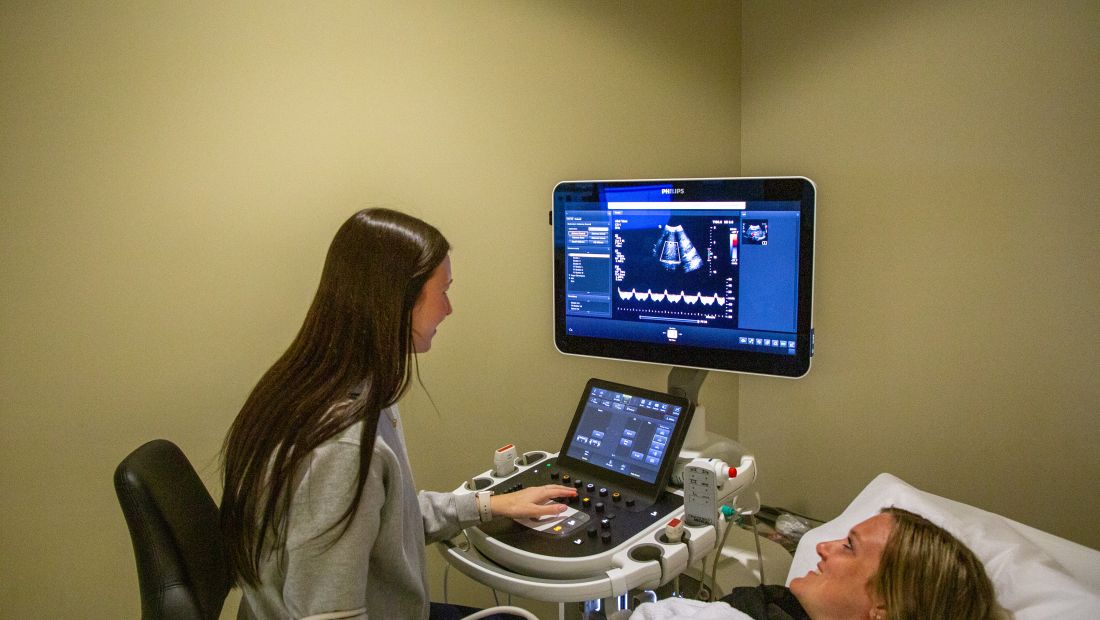 a sonographer is using an ultrasound machine in a hospital room to review scanning results with a patient