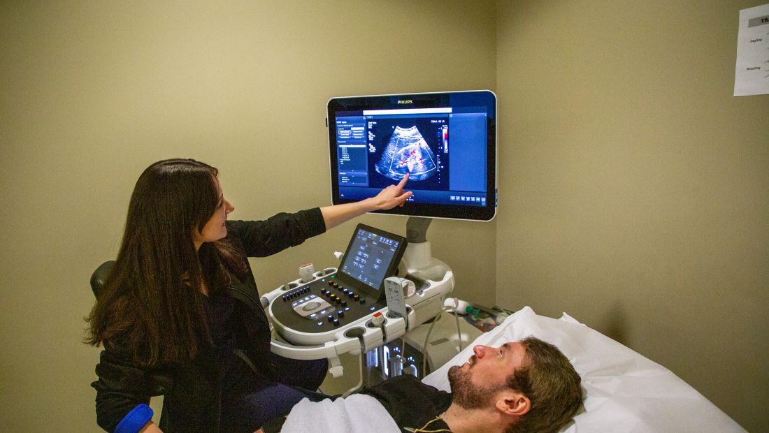 sonography student looking at scan of man's abdomen