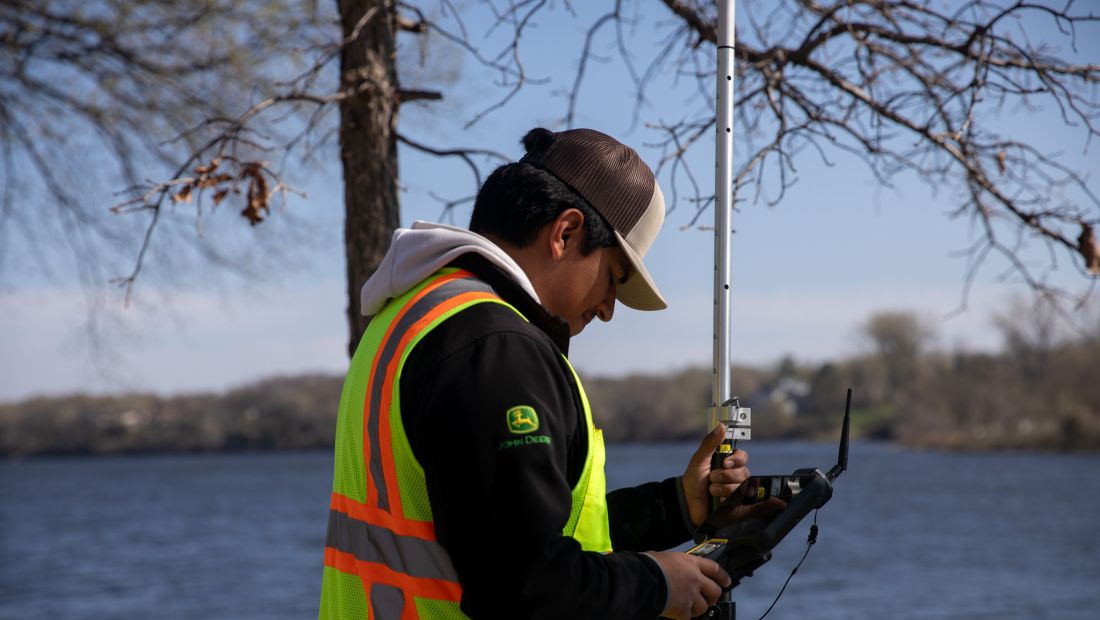 student checking screen of survey equipment, river in background