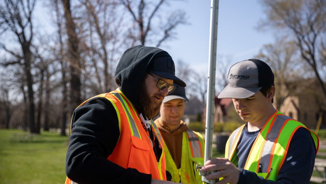instructor with students outside showing how to operate survey equipment