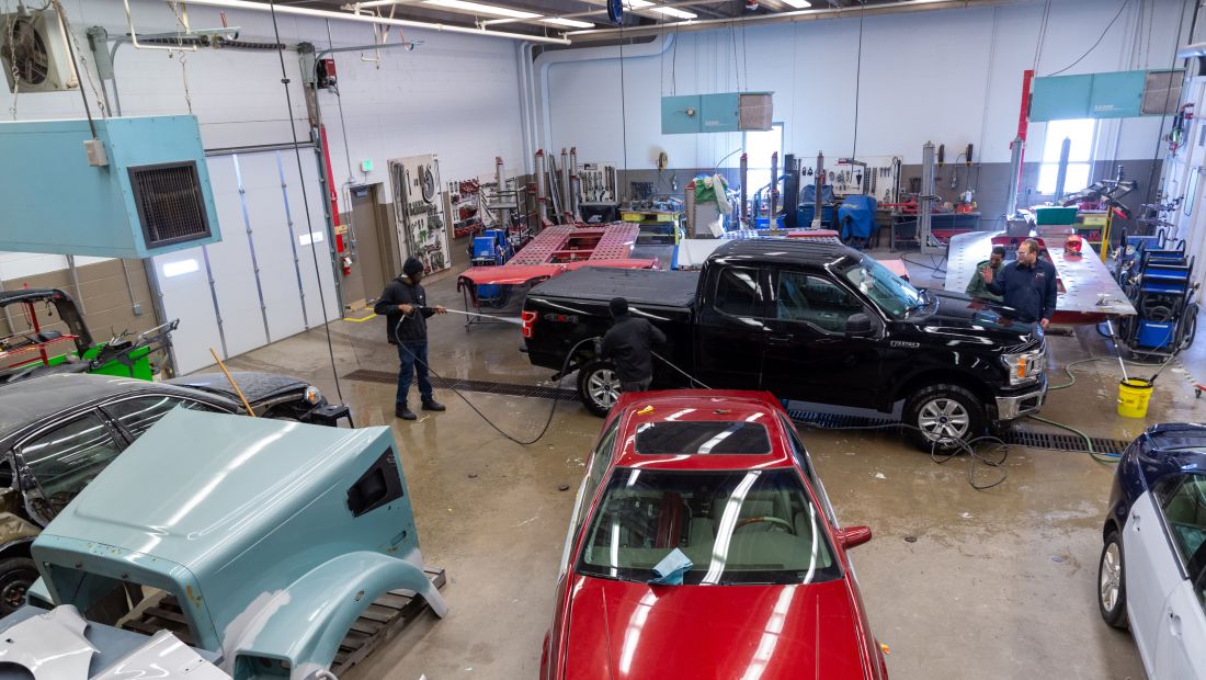 wide angle shot of Auto Body lab, showing multiple cars and students