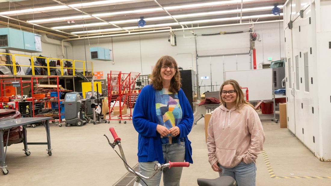 Mary and student stand next to freshly painted bike, smiling