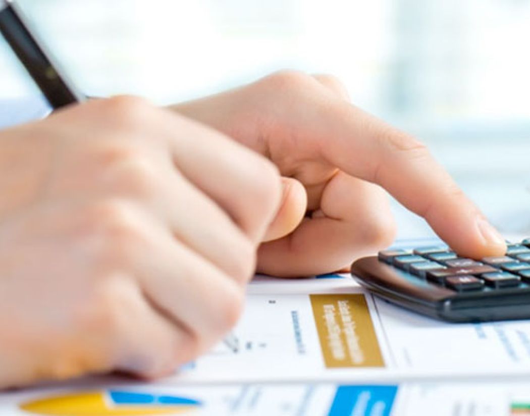 hands with pen and calculator resting on surface of paper forms