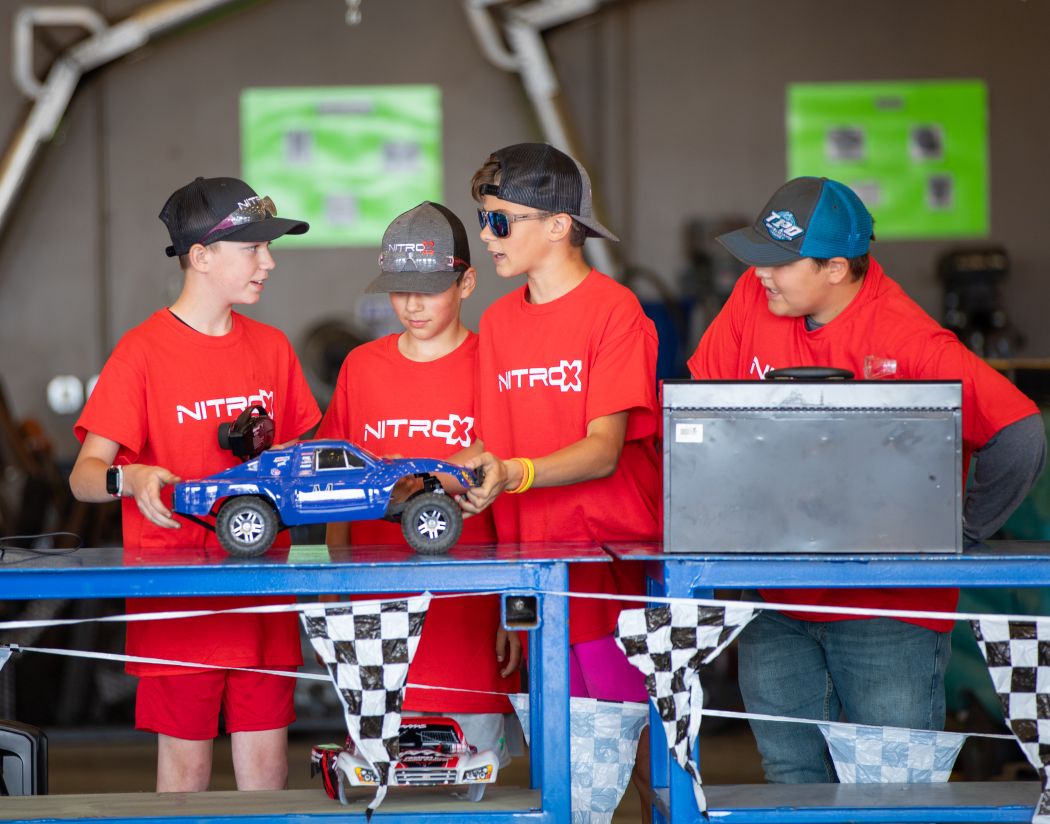 4 campers wearing Nitro-X shirts and hats working on a miniature car