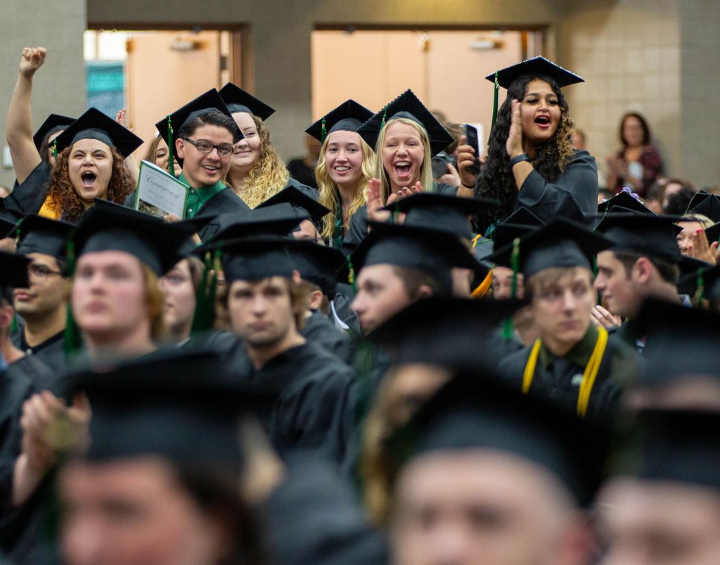 Students sitting at commencement with small group standing up and cheering