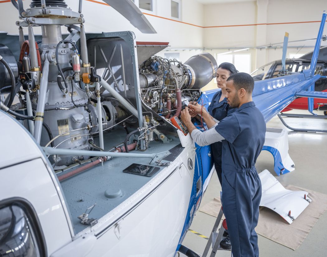 Two people working on the engine of a small aircraft in a hangar