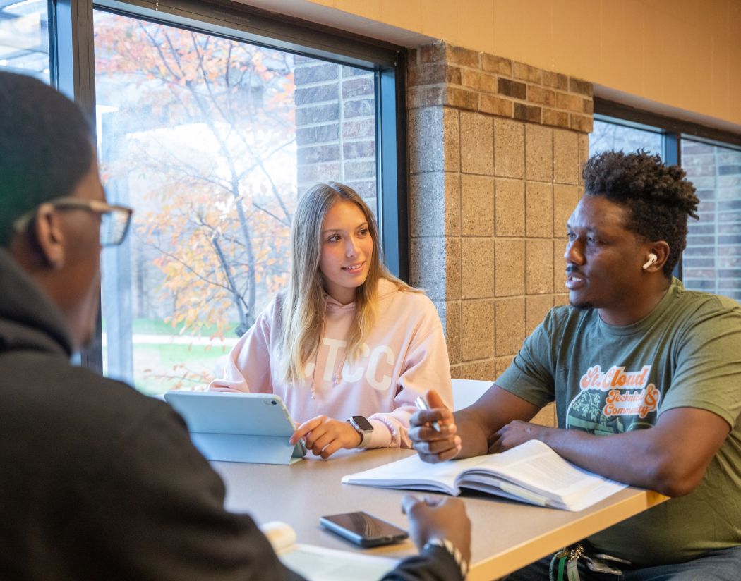 three students wearing sctcc gear sitting and talking next to a window