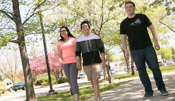 three students walking outside with a background of trees