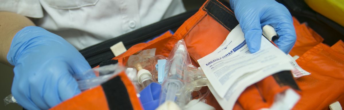 close up shot of gloved hands sorting through medical items in an orange bag