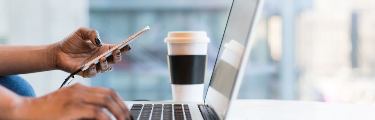 person typing into laptop and holding mobile phone in other hand
