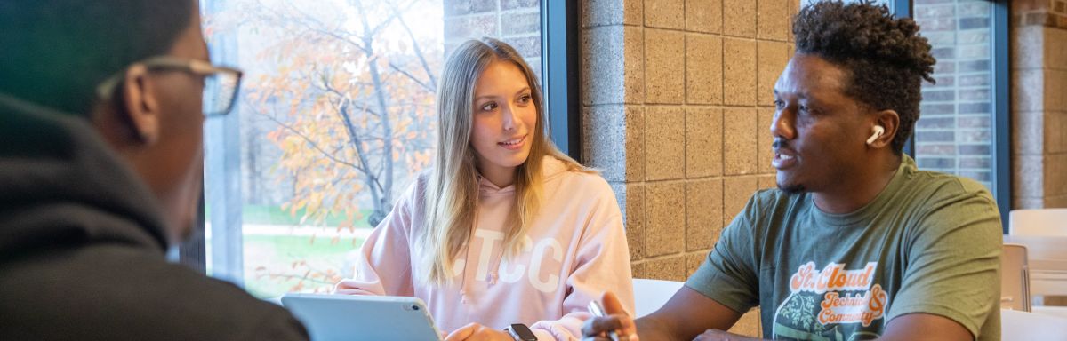 three students wearing sctcc gear sitting and talking next to a window 
