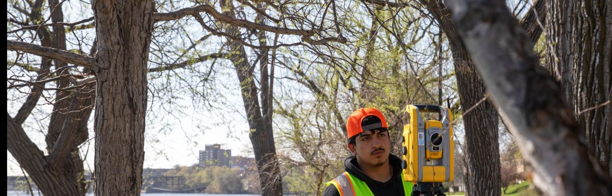 student at a river, framed by trees, surveying