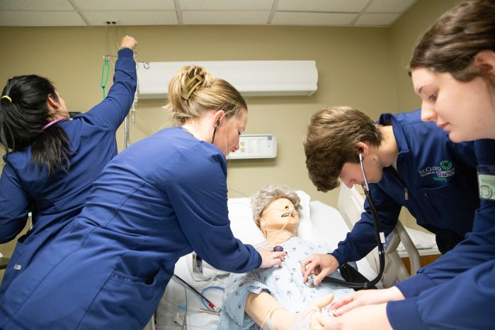 Four practical nursing students performing a medical exam on a simulation mannequin