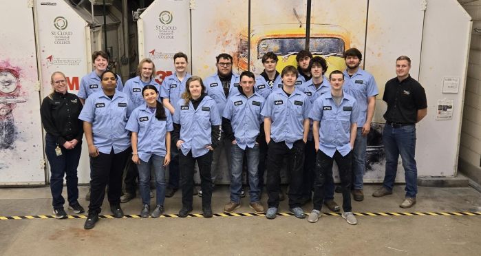 Auto body students in front of paint booths wearing donated blue shirts