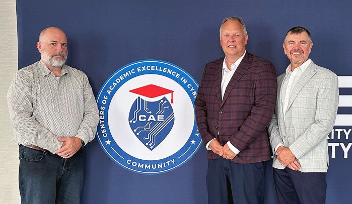 Brian Volkmuth with two SCSU faculty in front of the national cybersecurity logo