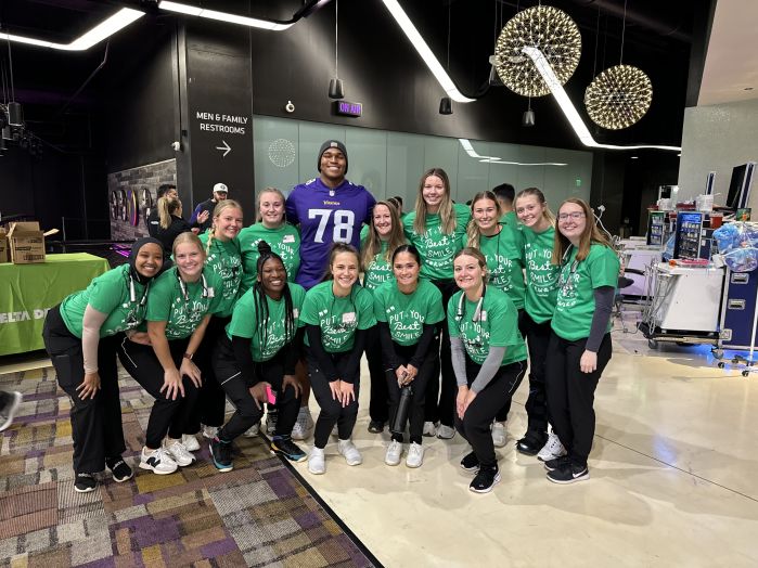 Dental hygiene students in two rows with MN Vikings player in back