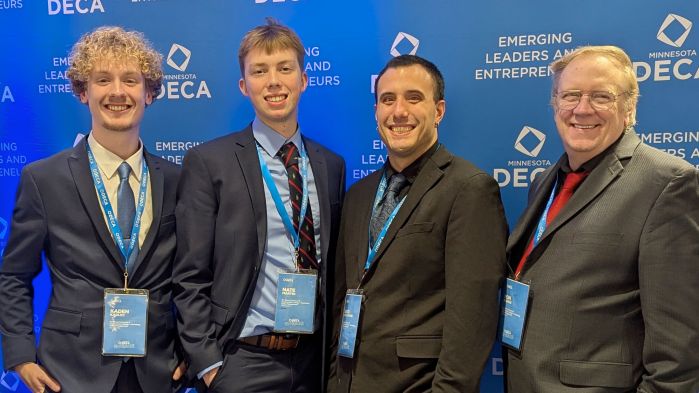 Four DECA members standing in front of the DECA backdrop