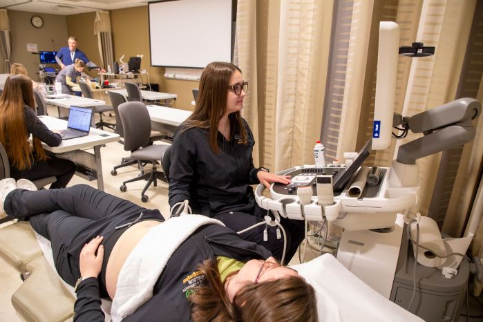 sonography students practicing on the ultrasound with class in background