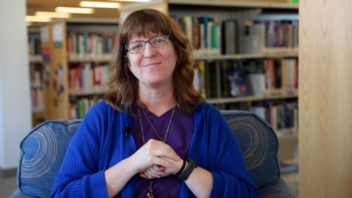 Mary Jordan sitting in front of shelving and smiling