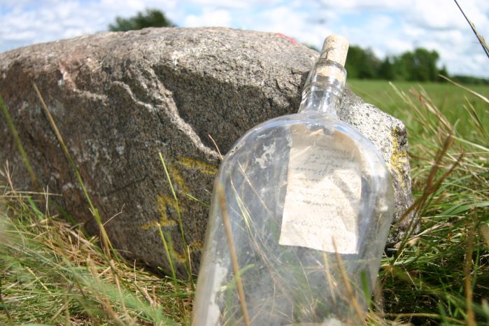 a literal message in a bottle! leaning against a rock in a field.