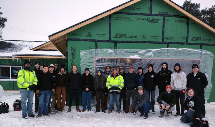 electrical students in a group smiling at camera in front of a house under construction