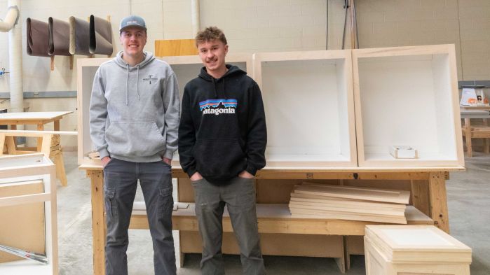 Two carpentry students smiling in front of cabinet projects