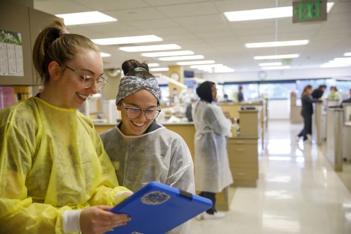 Two dental students look at a chart together with the dental clinic in the background