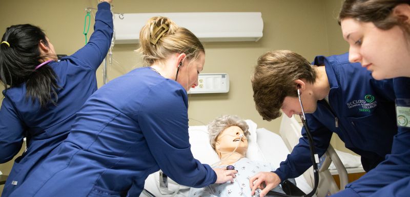 Four practical nursing students performing a medical exam on a simulation mannequin