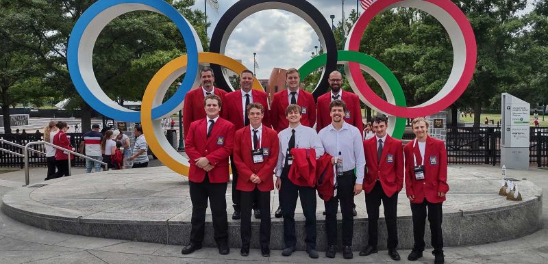 Group of students and instructors standing in front of olympic rings
