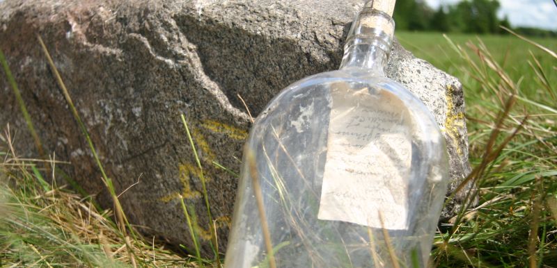 a literal message in a bottle! leaning against a rock in a field.