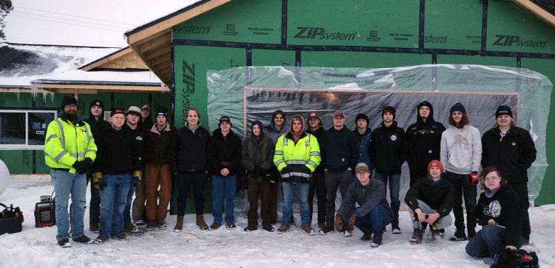 electrical students in a group smiling at camera in front of a house under construction
