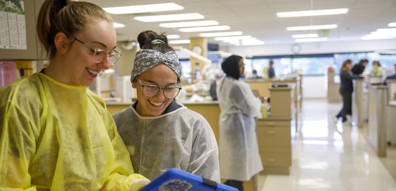 Two dental students look at a chart together with the dental clinic in the background