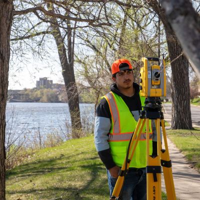 student at a river, framed by trees, surveying
