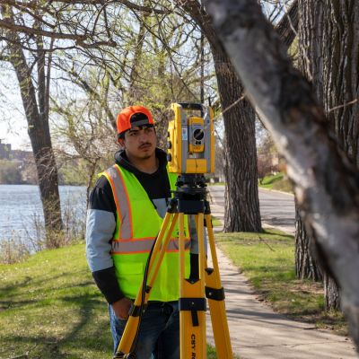 student at a river, framed by trees, surveying