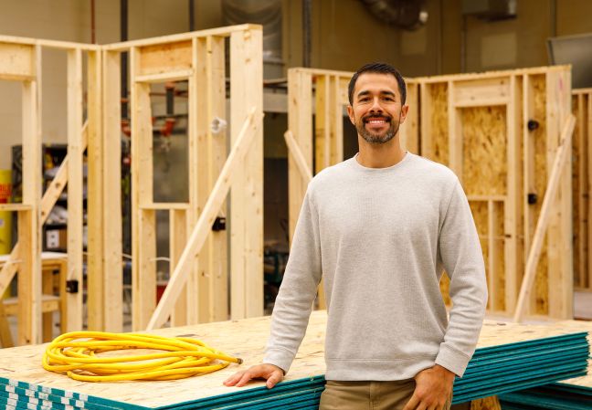 Trevor Ford stands in the carpentry lab with constructed walls behind him
