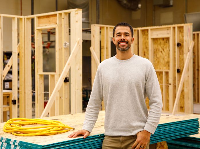 Trevor Ford stands in the carpentry lab with constructed walls behind him
