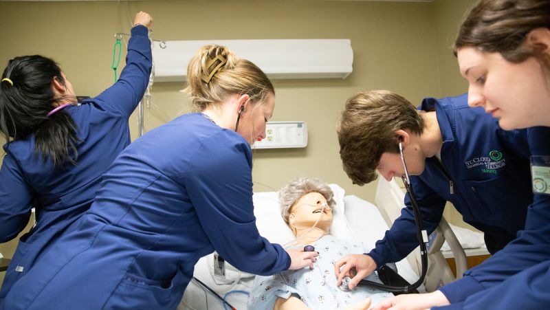 Four practical nursing students performing a medical exam on a simulation mannequin