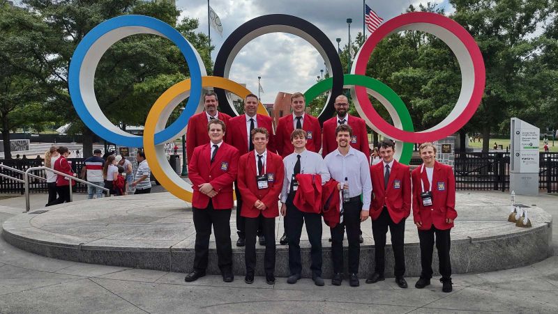 Group of students and instructors standing in front of olympic rings