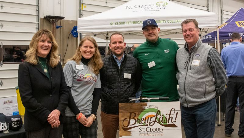 Five attendees at brewlash smiling at camera in front of tent in MHT lab. Daniel Larson is fourth from left.