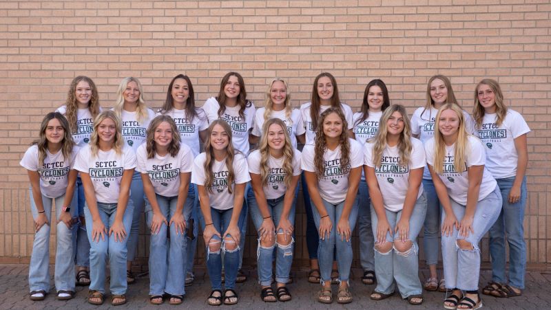volleyball team in two rows against brick wall