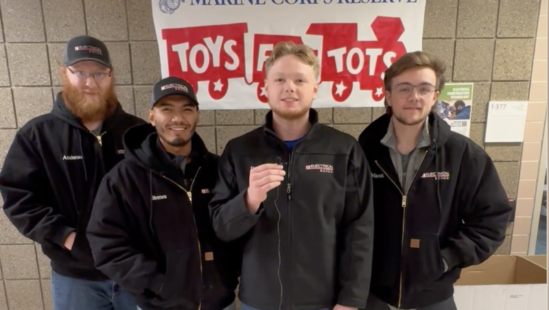 Mesa members in a row with Toys for Tots banner