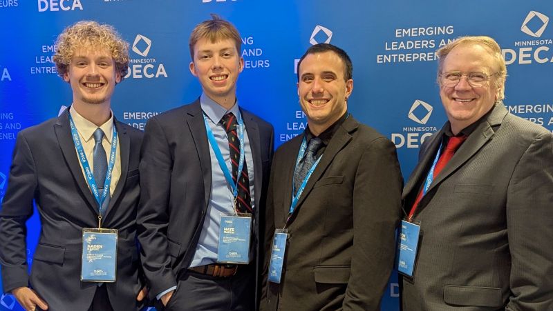 Four DECA members standing in front of the DECA backdrop