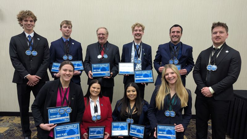DECA students in two rows with medals and plaques