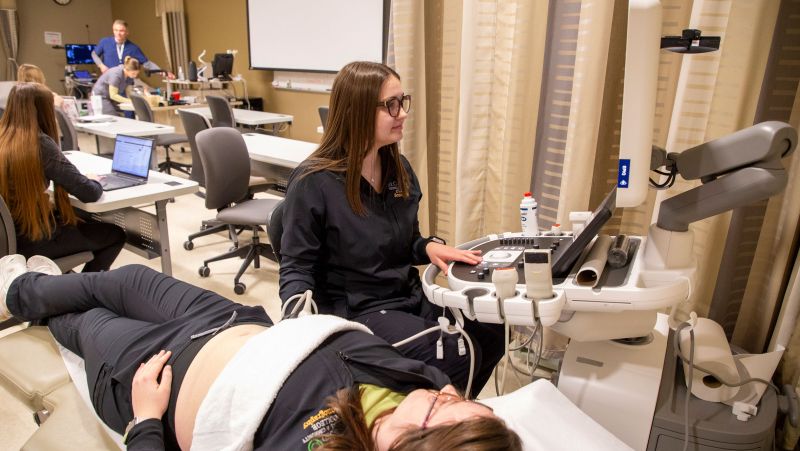 sonography students practicing on the ultrasound with class in background