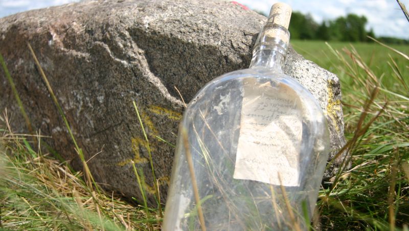 a literal message in a bottle! leaning against a rock in a field.