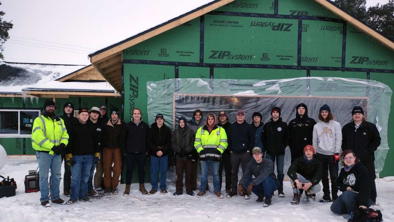 electrical students in a group smiling at camera in front of a house under construction