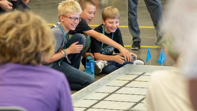 students excitedly pointing at robot competition field 