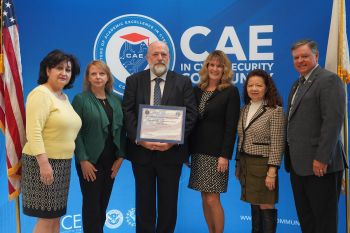 6 people on stage receiving designation with CAE in background